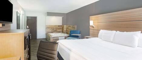 Habitación de hotel moderna con una cama grande, un escritorio, una silla, un televisor y un baño con bañera, además de una pared de acento de piedra.