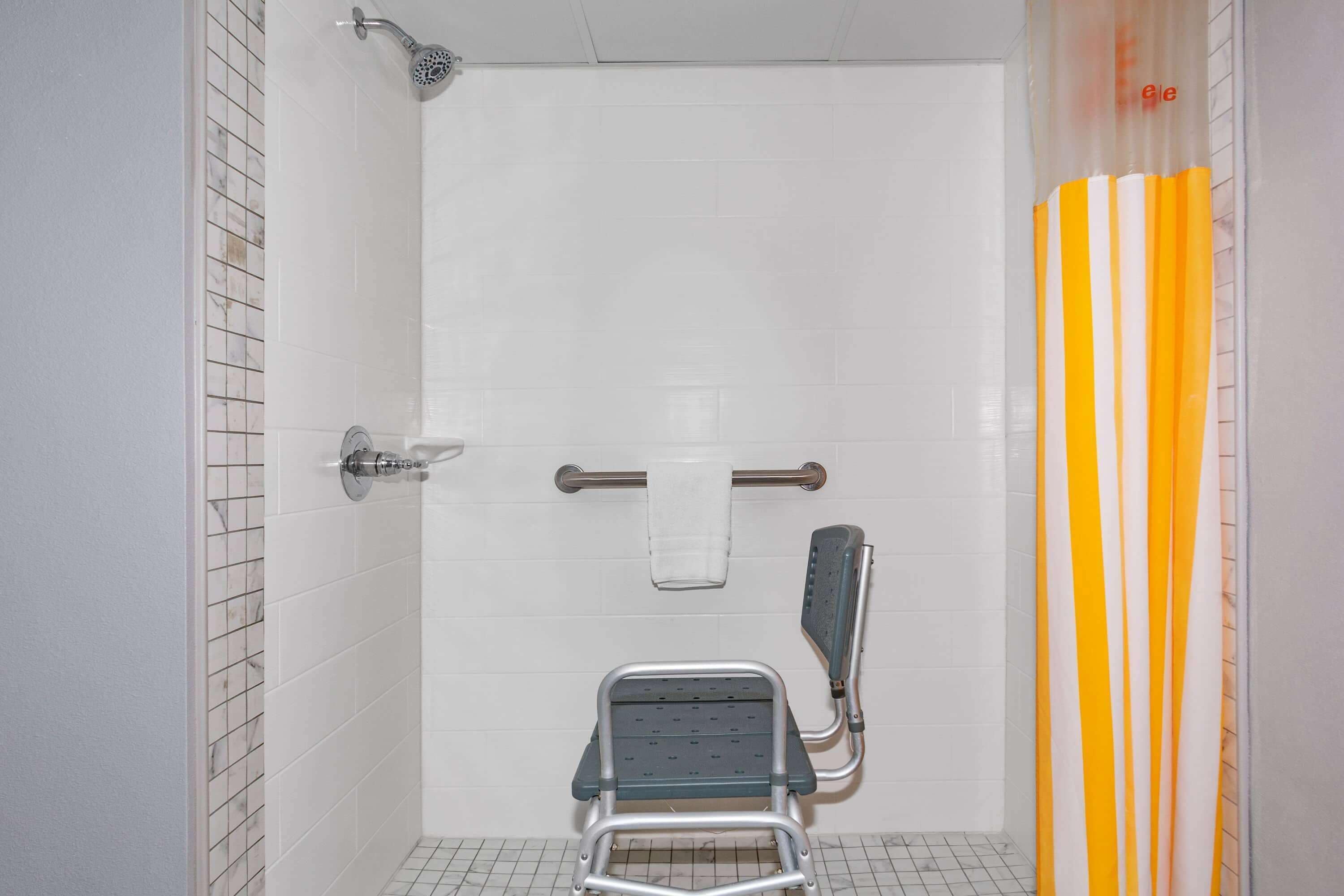 A bathroom with a shower, a grab bar, a wheelchair-accessible bench, and a striped shower curtain.