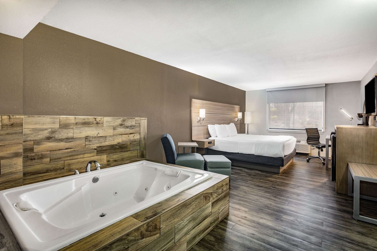 A modern hotel room with a large bathtub, a bed, a desk, and a chair.