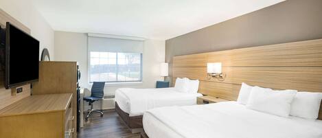 A hotel room with two beds, a desk, a TV, and a window with a view.