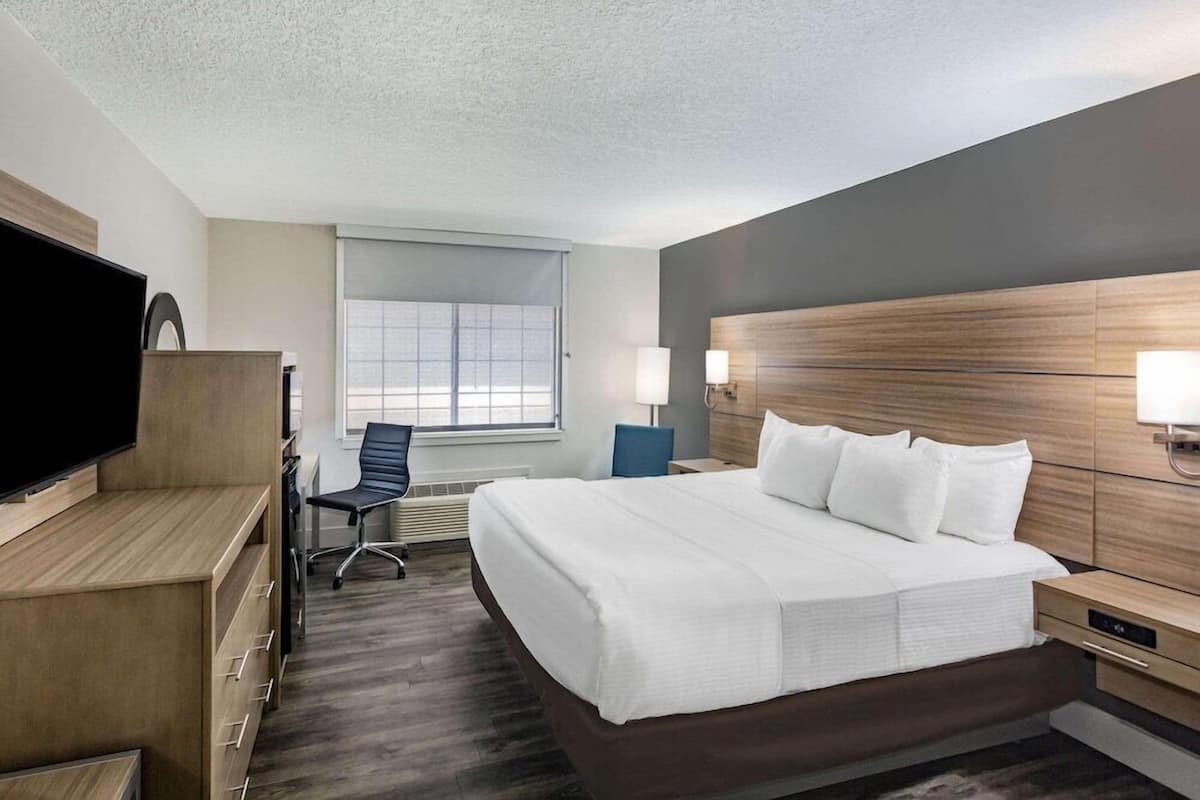 A hotel room with a bed, desk, chair, TV, and window.