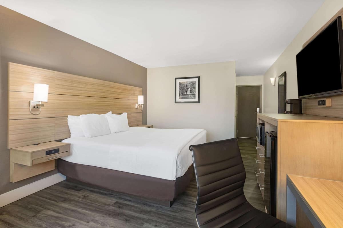 A hotel room with a large bed, bedside tables, a desk with a chair, a flat-screen TV, and a framed picture on the wall.