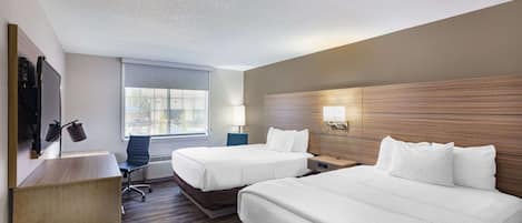 Habitación de hotel con dos camas, un escritorio, una silla, un televisor y un ventanal.