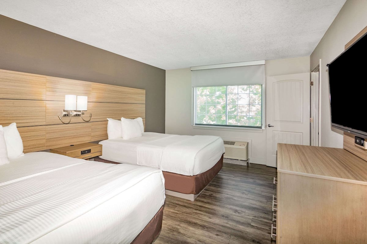 A hotel room with two beds, a TV, a window, and a door.