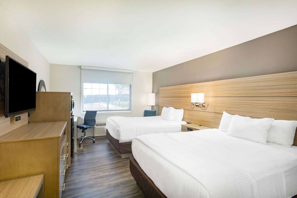 A hotel room with two beds, a desk, a chair, a television, and a window.
