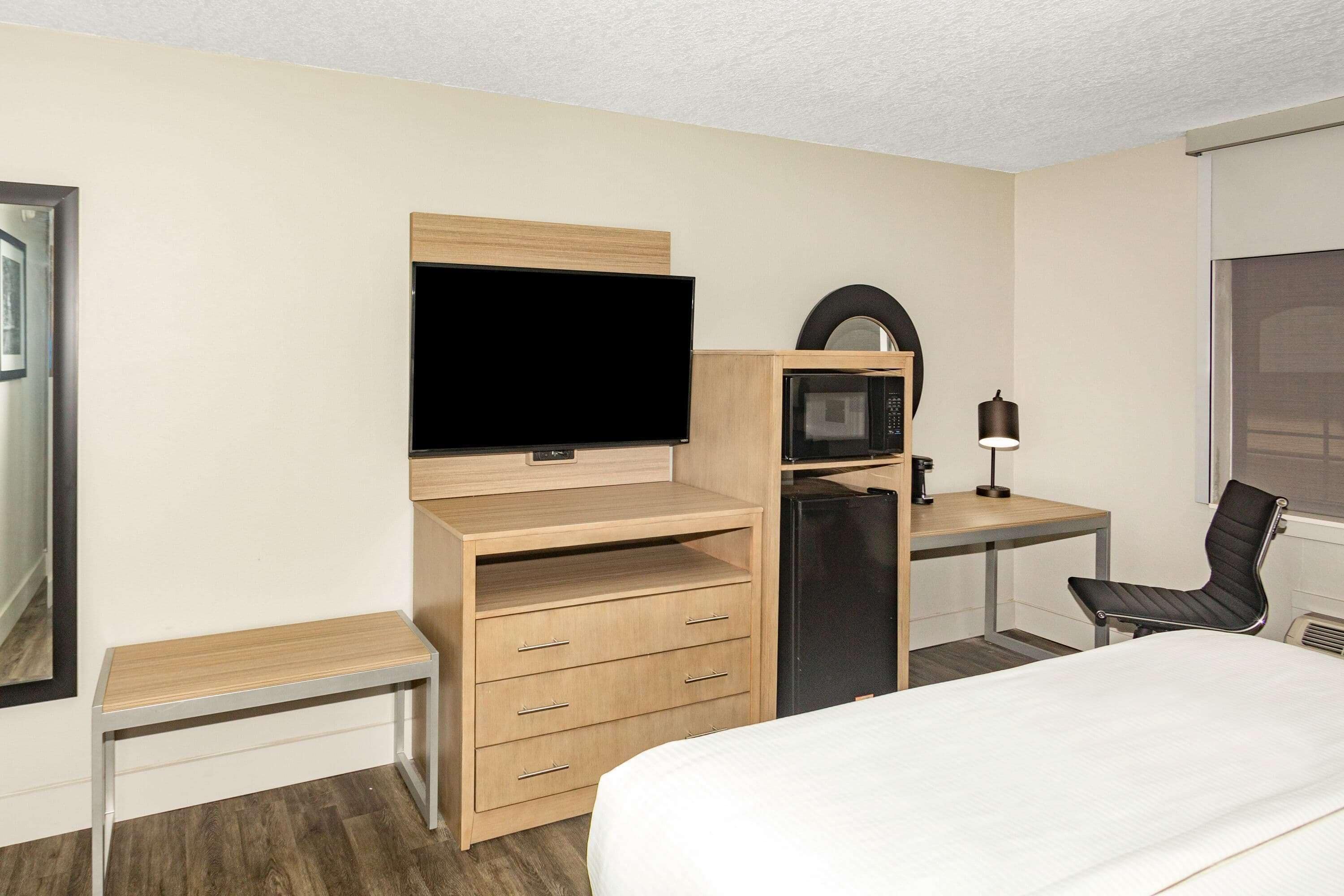 A hotel room with a bed, a desk with a computer, a television, a microwave, and a chair.