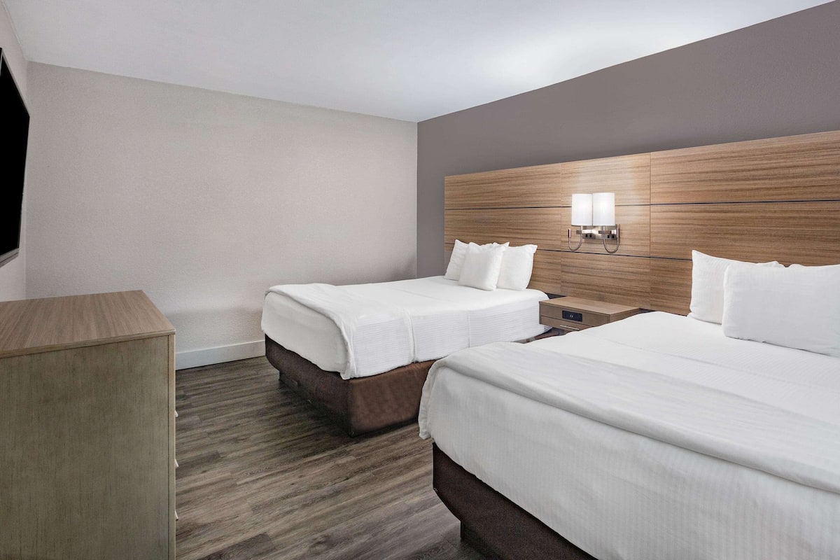 A hotel room with two beds, a wooden headboard, a nightstand, and a TV.