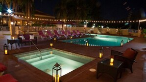 A pool area with lounge chairs and tables, surrounded by string lights.