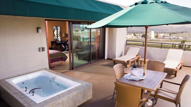 A balcony with a hot tub, lounge chairs, and a table with an umbrella. - Airtel Plaza Hotel (Van Nuys)