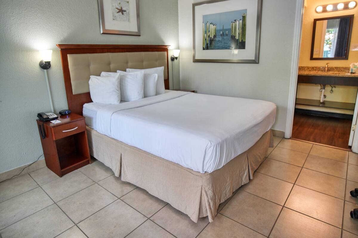 Hotelkamer met een groot bed, een nachtkastje met telefoon en notitieboekje, een ingelijst schilderij aan de muur, en een badkamer zichtbaar door een geopende deur.