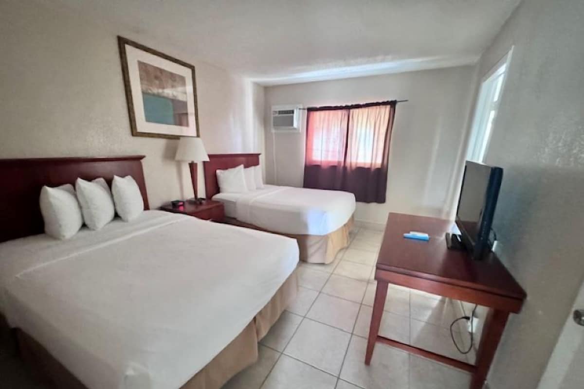 A hotel room with two beds, a TV, a lamp, and a window with curtains.