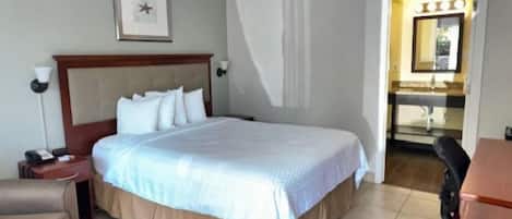 Una habitación de hotel con una cama grande, una mesita de noche, una silla y un baño visible a través de una puerta abierta.