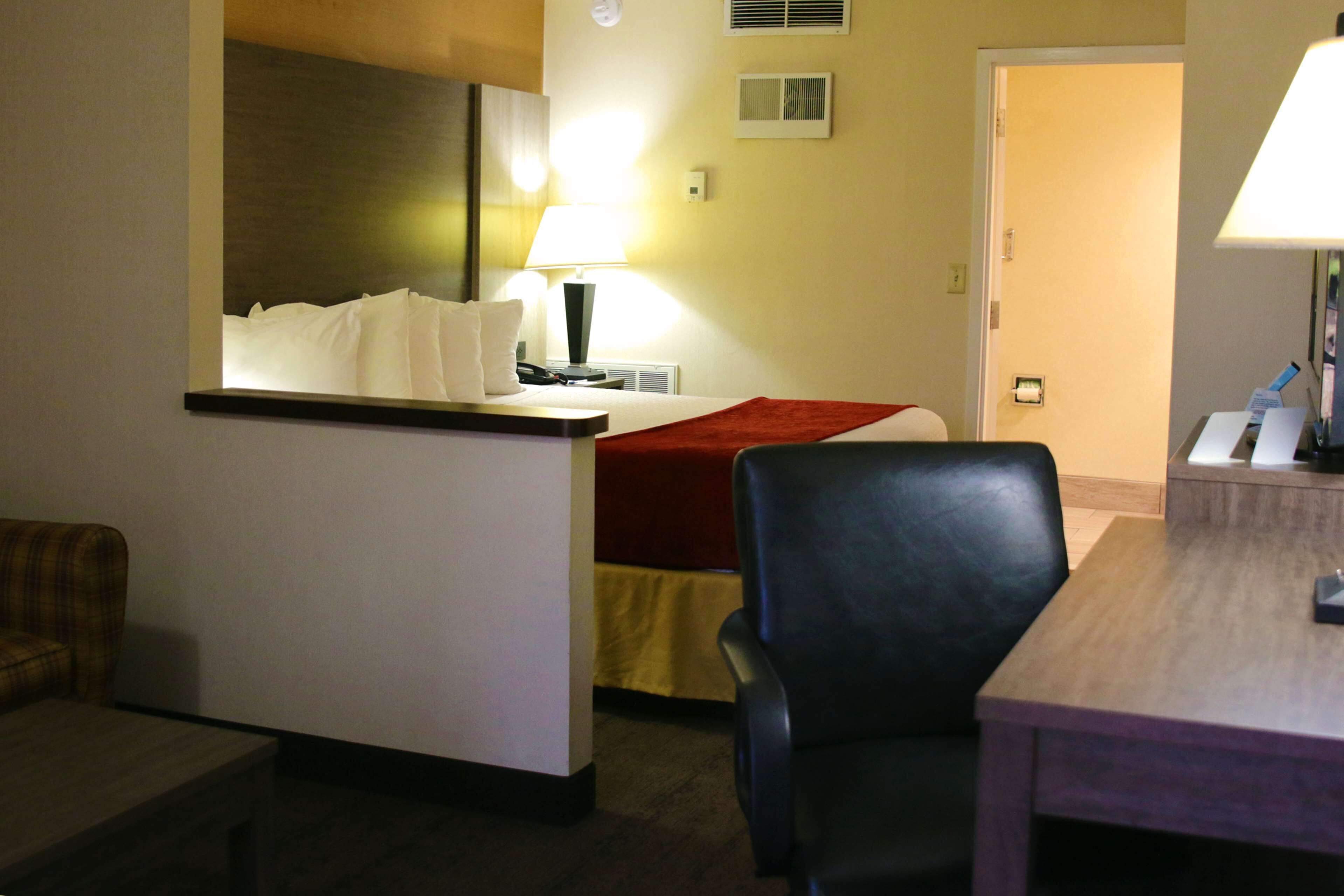 A hotel room with a bed, a desk, a chair, a lamp, and a couch.