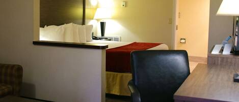 A hotel room with a bed, a desk, a chair, a lamp, and a couch.