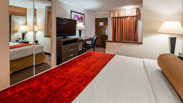 A hotel room with a bed, a desk with a television, a chair, and a window with curtains.