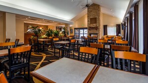 A restaurant with multiple tables and chairs, a stone fireplace, and potted plants.