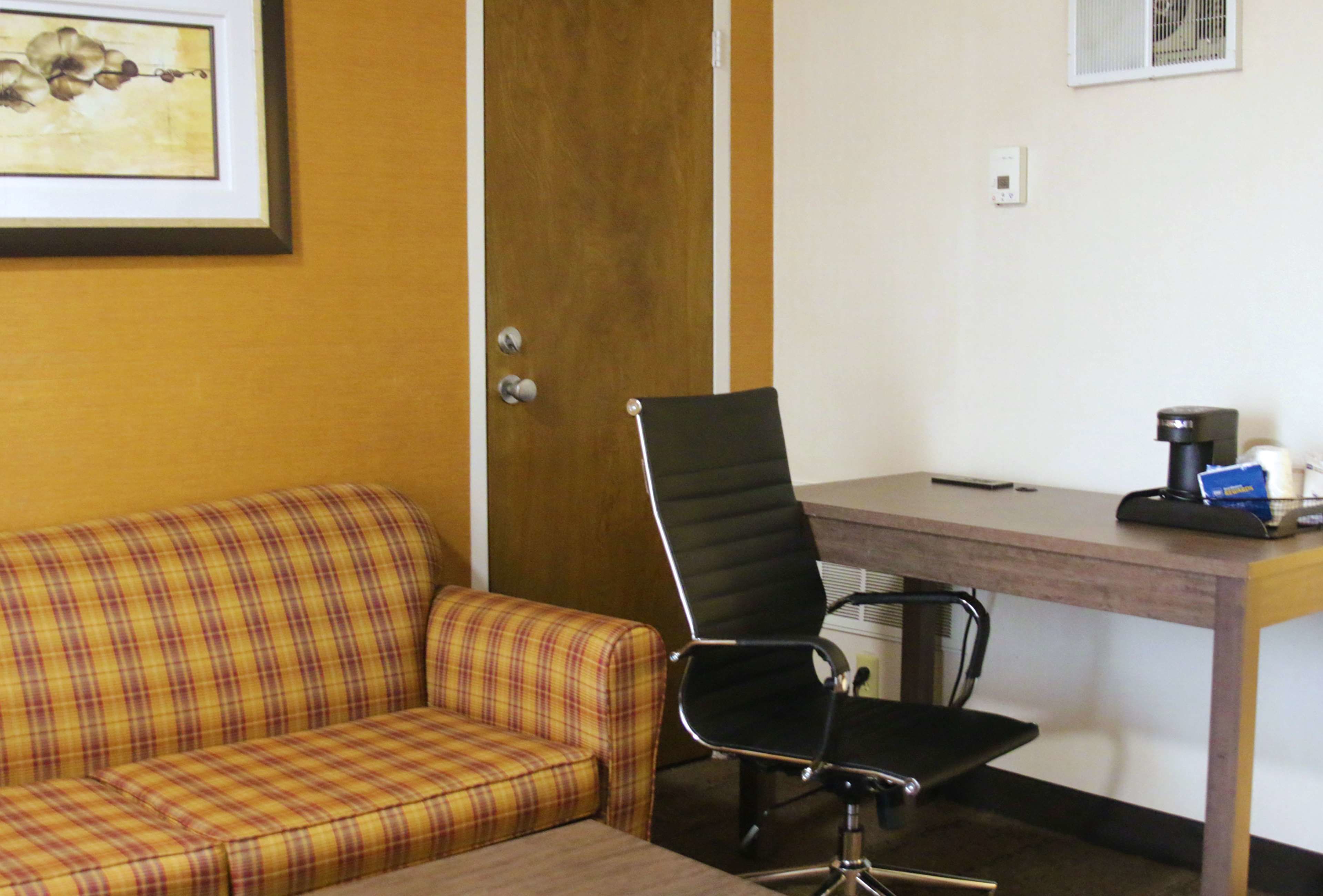 A room with a plaid sofa, a black office chair, a wooden desk, and a framed picture on the wall.