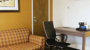 A room with a plaid sofa, a black office chair, a wooden desk, and a framed picture on the wall.