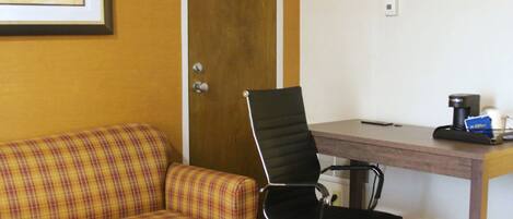 A room with a plaid sofa, a black office chair, a wooden desk, and a framed picture on the wall.