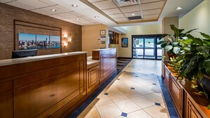 A reception area with a wooden reception desk, a cityscape painting, and a tiled floor.