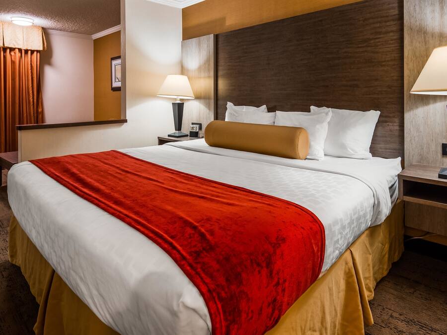 A hotel room with a large bed, two bedside tables, a nightstand, a red throw blanket, and two lamps.