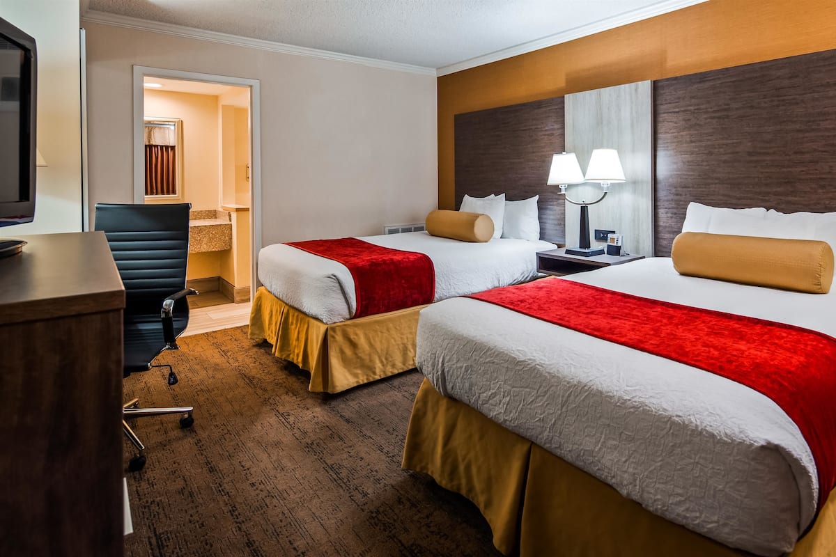 A hotel room with two beds, a desk, a chair, and a television.
