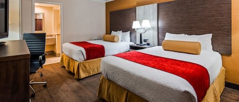 A hotel room with two beds, a desk, a chair, and a television.