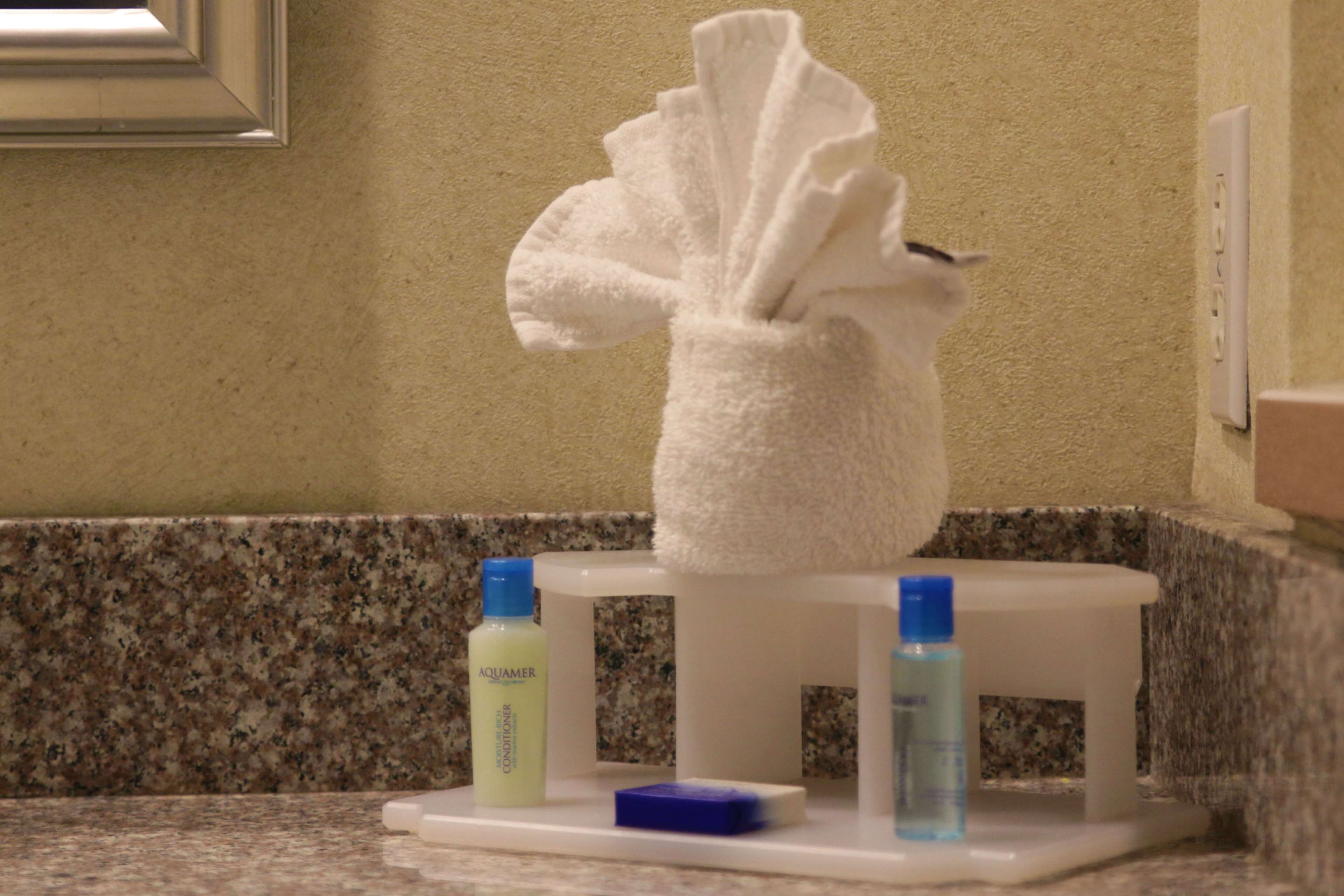 A bathroom with a towel rack holding a white towel, a bottle of Aquamere conditioner, and a bottle of blue liquid soap.