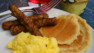 A plate with scrambled eggs, pancakes, sausages, and a glass of red beverage.
