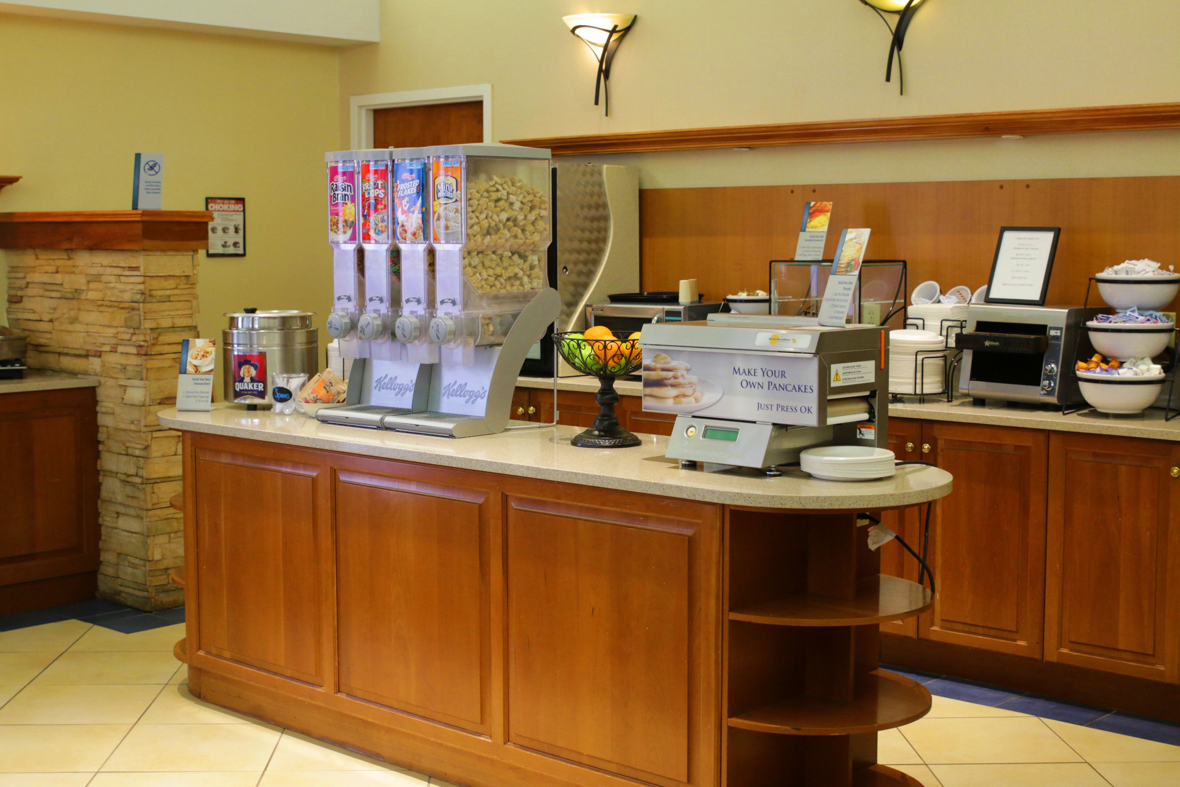 A hotel breakfast bar with a coffee machine, cereal dispenser, and a fruit bowl.