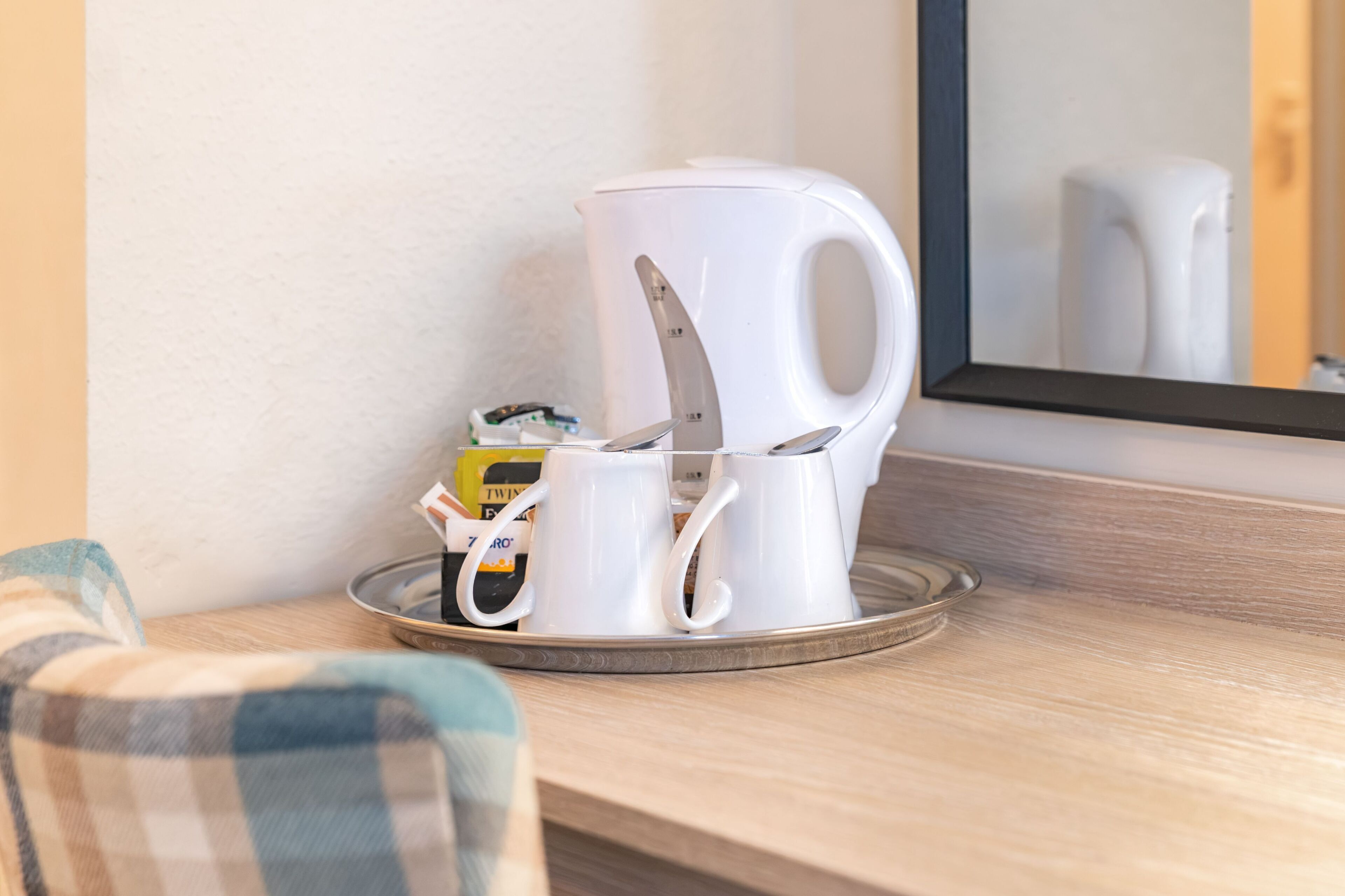 A coffee maker and a mug on a tray, with a chair and a mirror in the background.