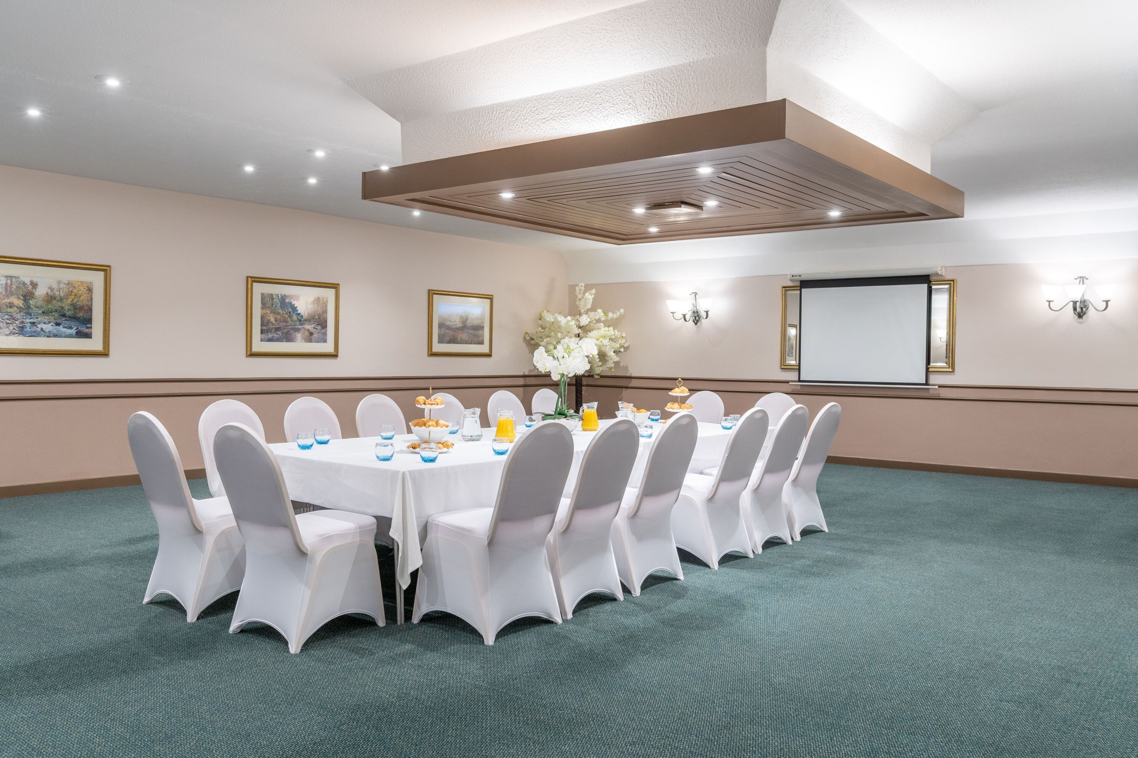 A conference room with a round table, white chairs, and a projector screen.