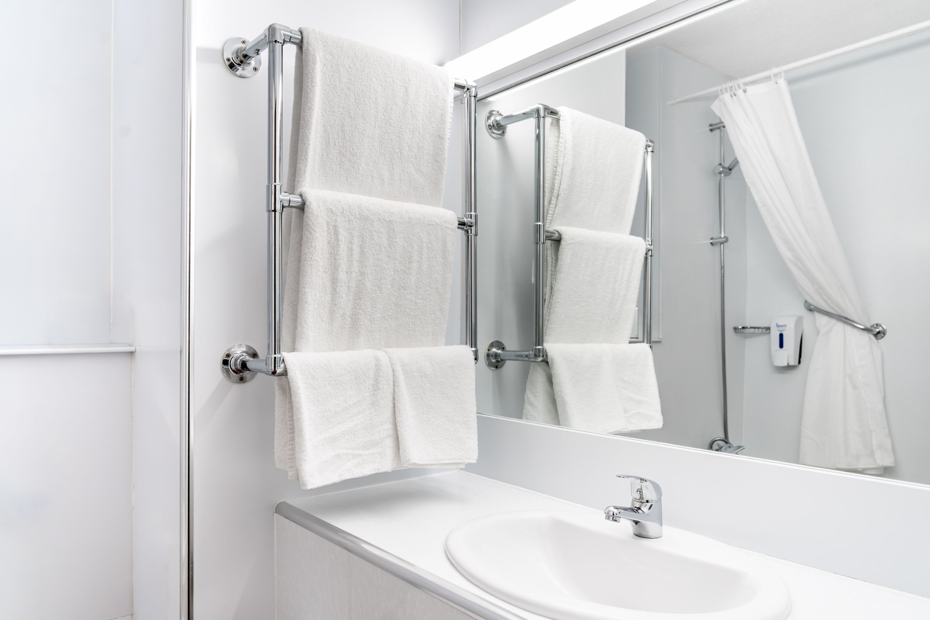 Een badkamer met een witte wastafel, chroombeslag en een spiegel die uitkijkt op de douche.