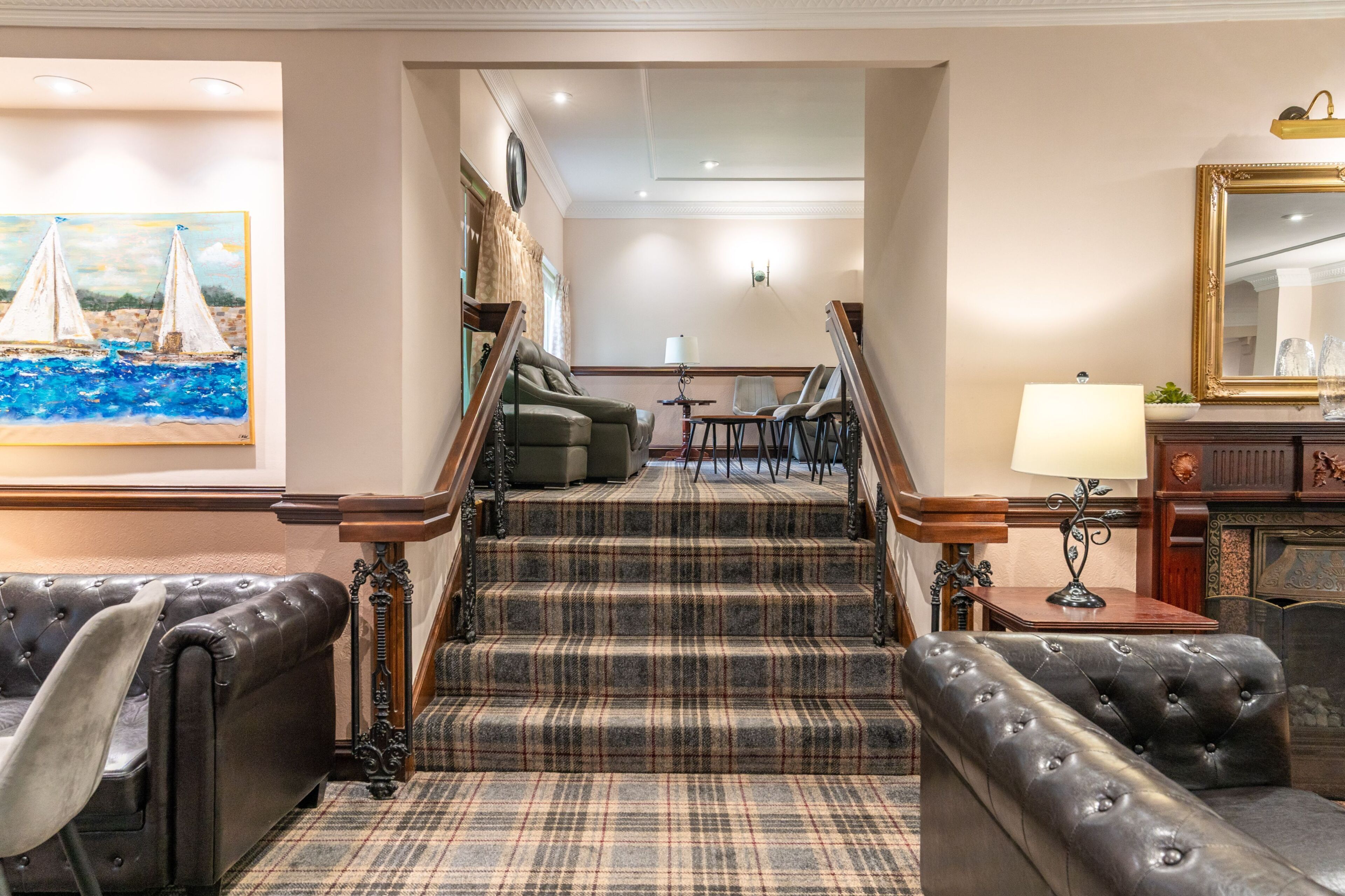 A hotel lobby with a staircase, a painting of sailboats, and a mirror.