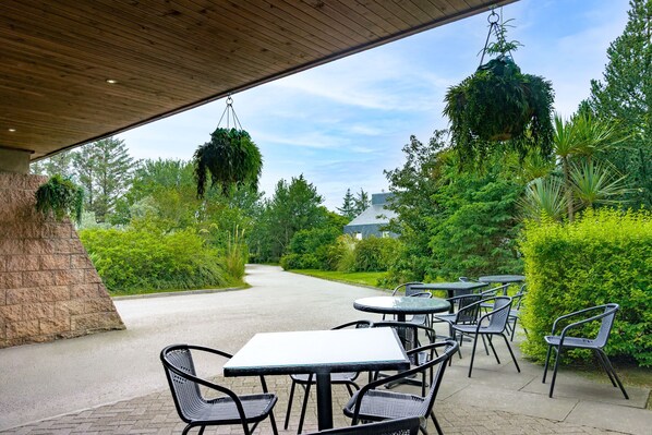 An outdoor patio with tables and chairs, surrounded by greenery and a pathway leading to a building. - The Waterside Hotel (Peterhead)