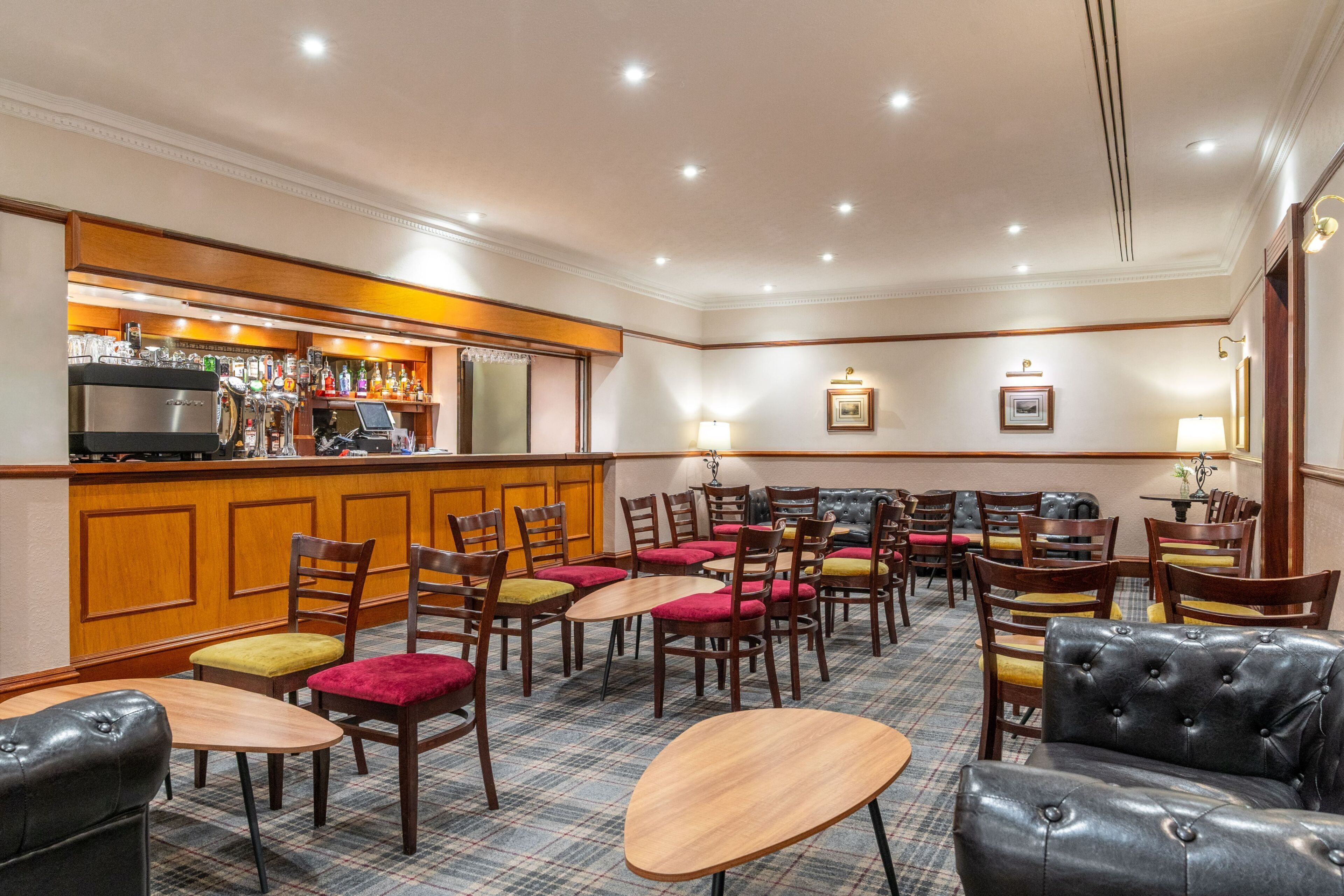 A hotel lobby with a bar area, multiple seating options including tables and chairs, and a check-in counter.