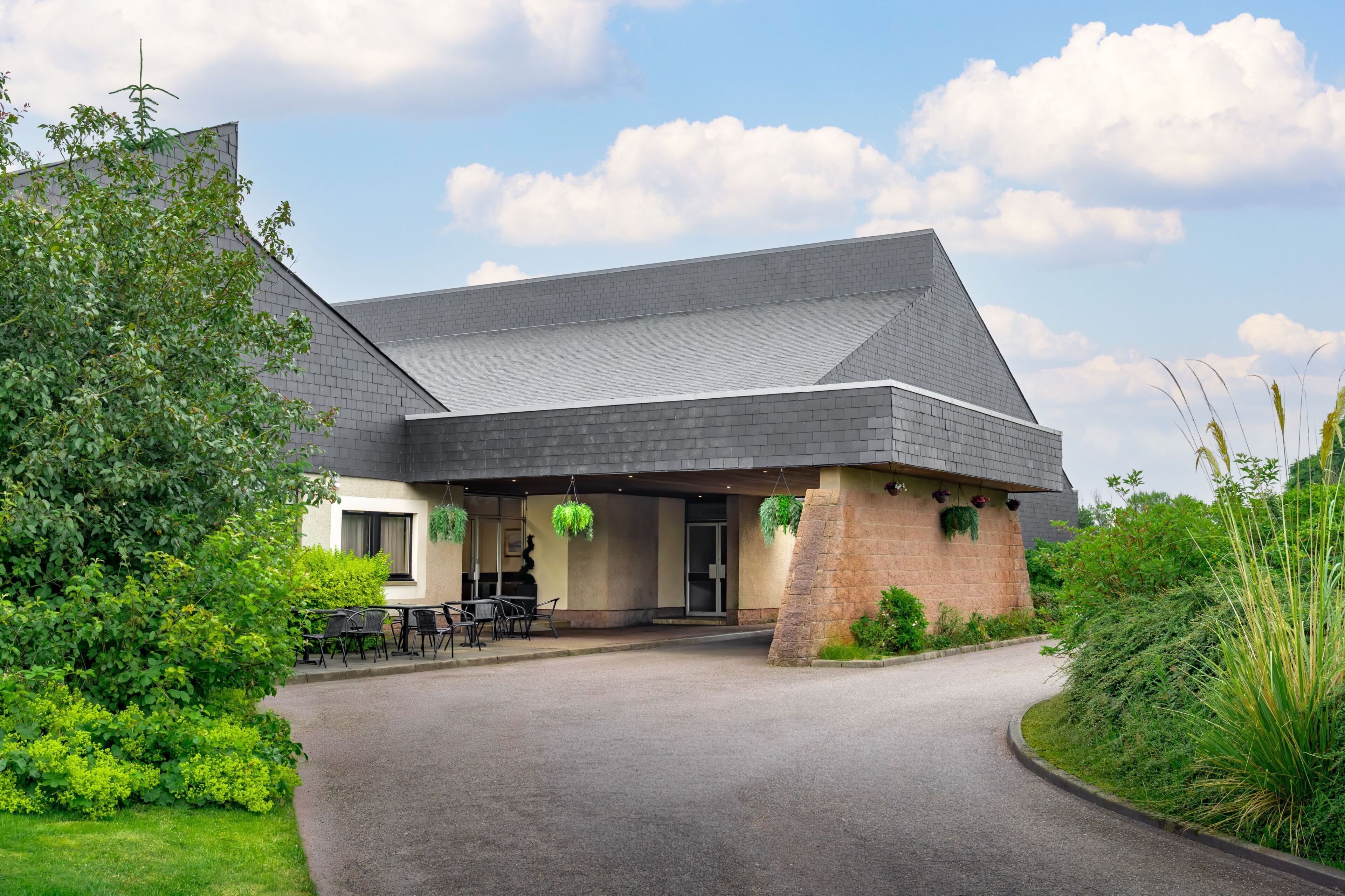A building with a sloped roof, a covered entrance area with outdoor seating, and a paved driveway.