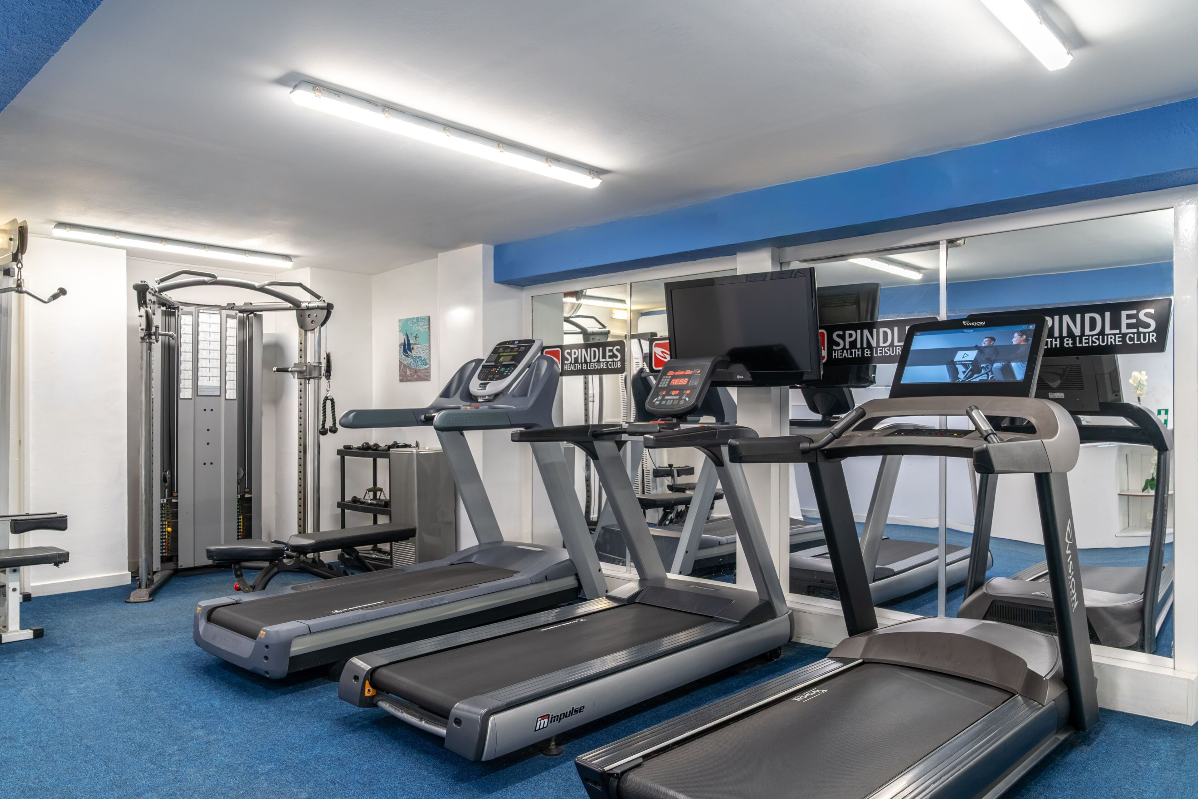 Un gimnasio con cintas de correr, máquinas de pesas y una televisión montada en la pared.