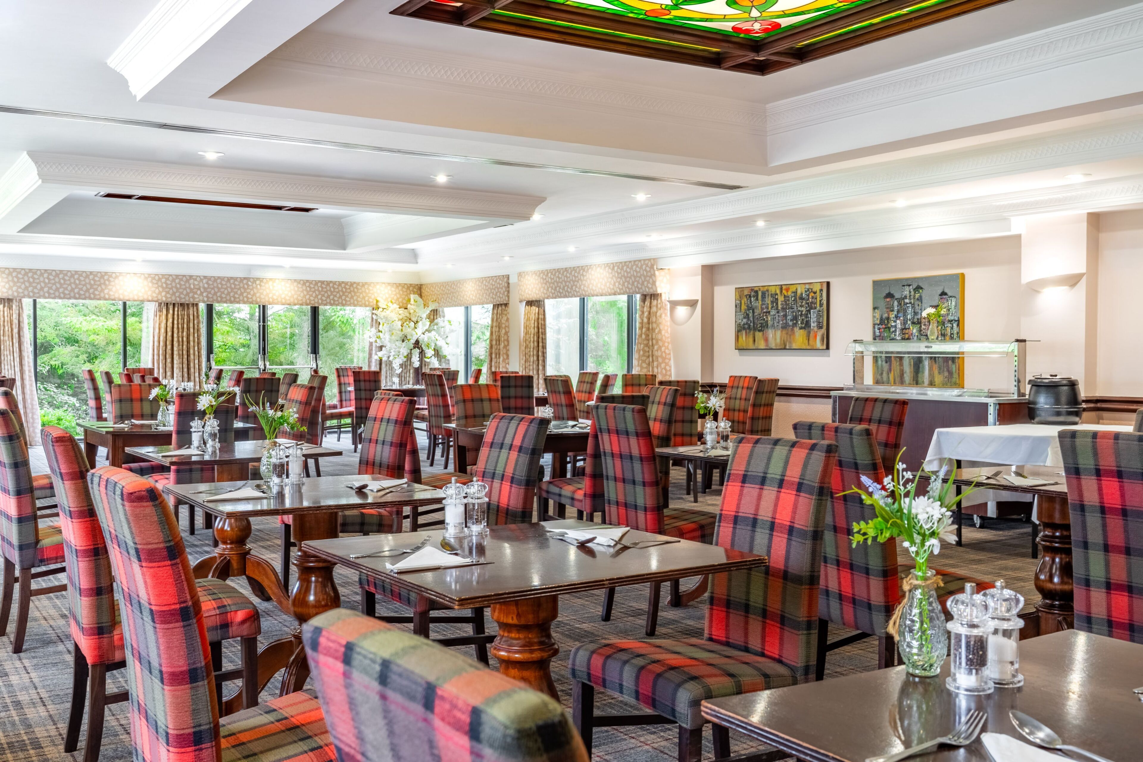 Un restaurant doté de nombreuses tables et chaises, de grandes fenêtres et d’un plafond en vitrail.
