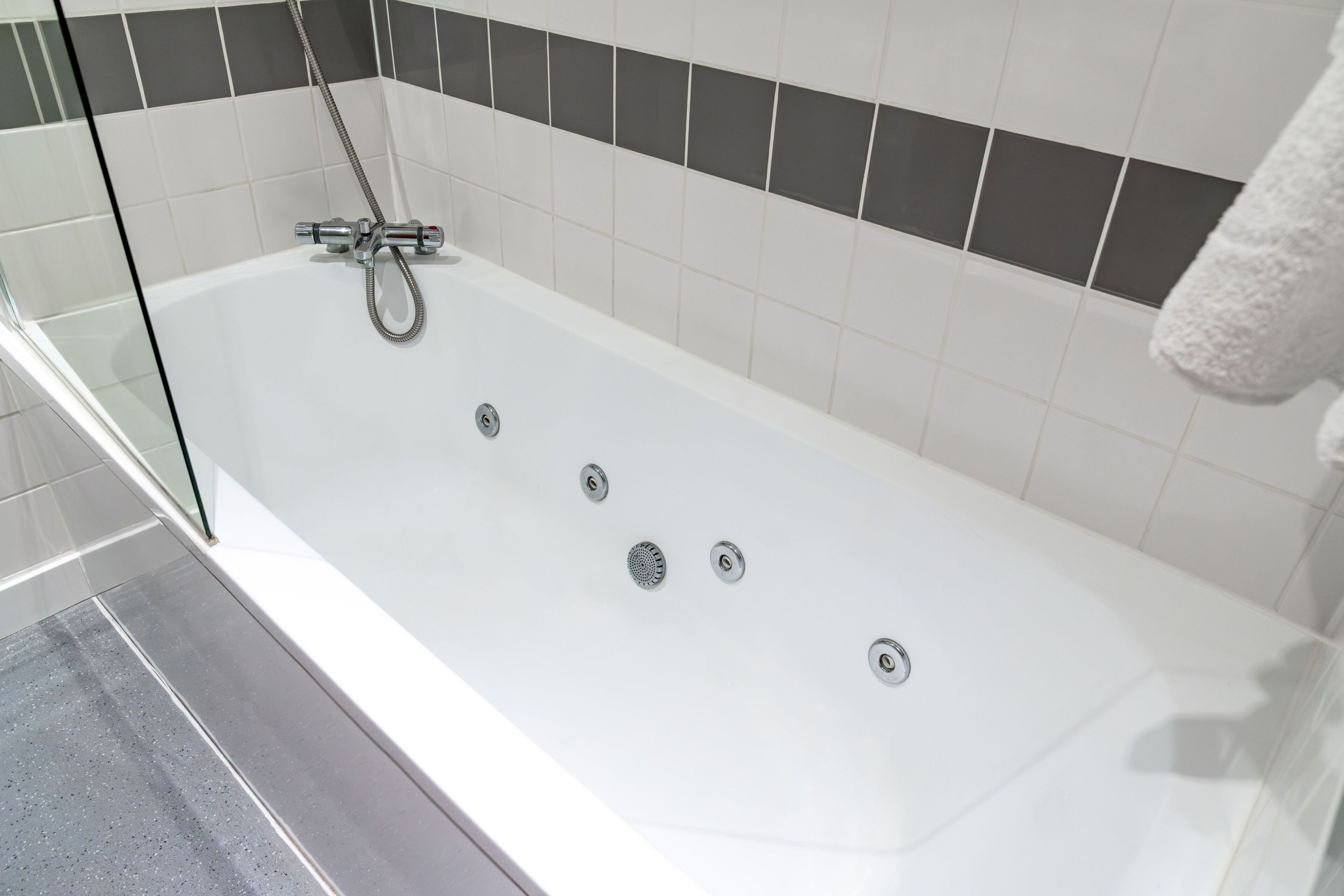 A modern bathroom with a white bathtub, a glass shower enclosure, and a tiled wall with a black and white pattern.