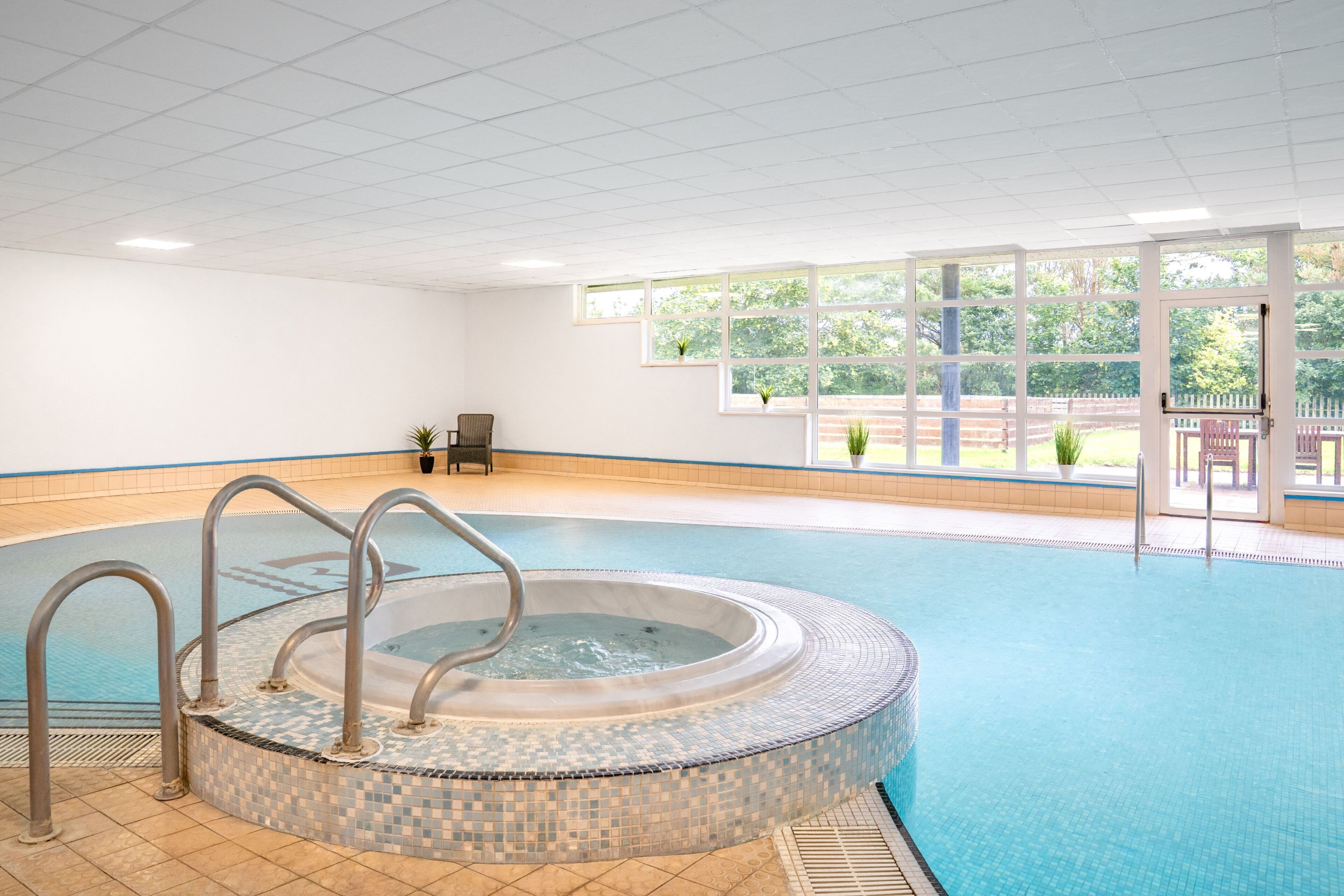 Una piscina con borde de azulejos, un jacuzzi y vistas al exterior a través de amplios ventanales.