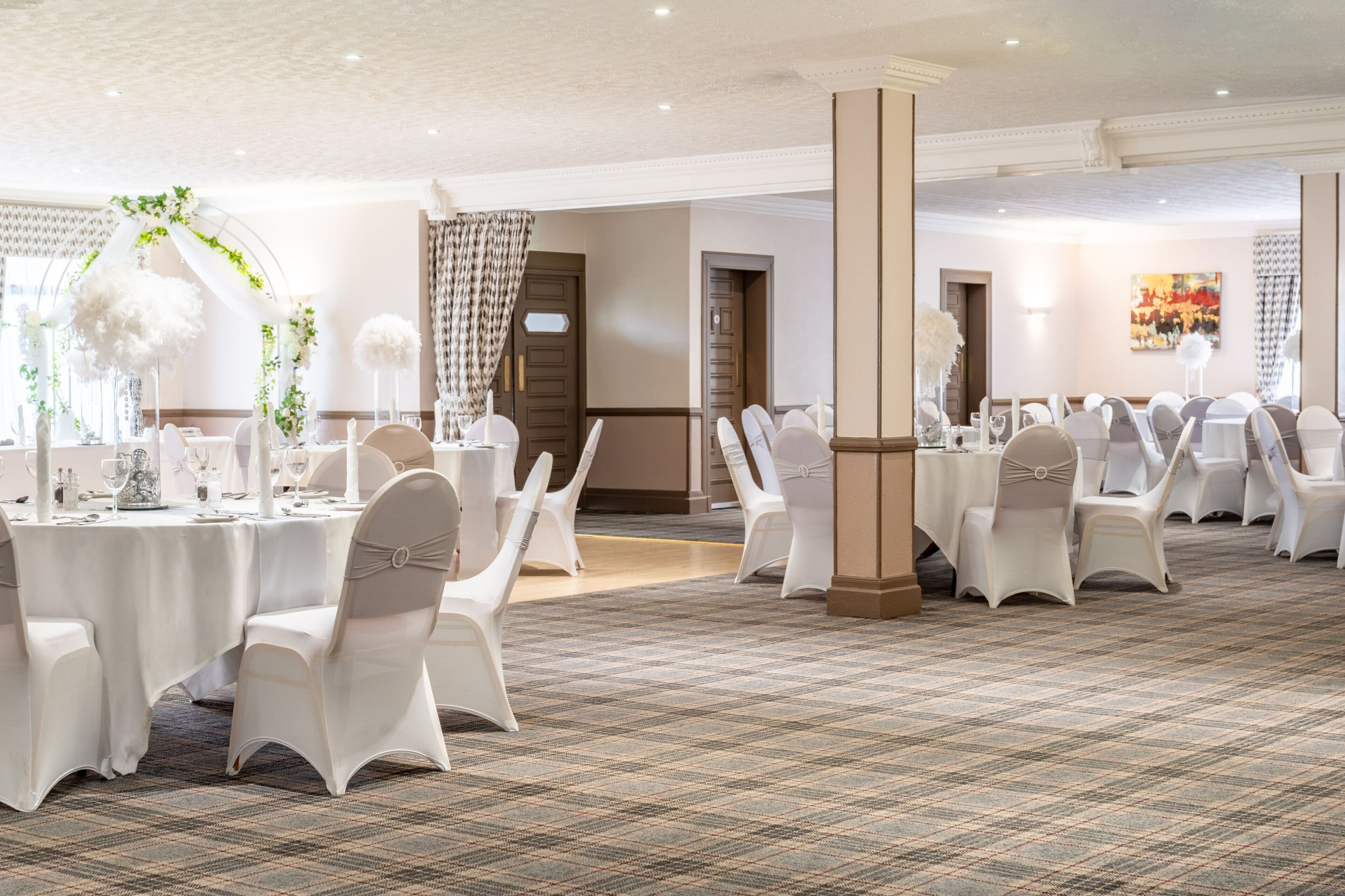 A banquet hall with round tables, white chairs, and a carpeted floor.