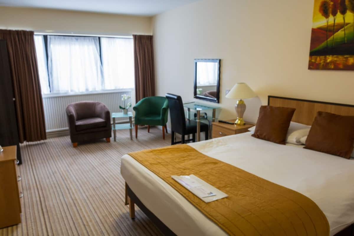 Hotellihuone, jossa on sänky, työpöytä, tuoli, lamppu ja taulu seinällä.