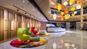 Een moderne hotel lobby met een receptiebalie, kleurrijke zitplaatsen en hangende sferische lampen.