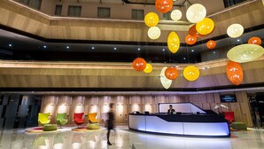 Een hotellobby met een receptiebalie, meerdere zithoeken en een moderne kroonluchter.