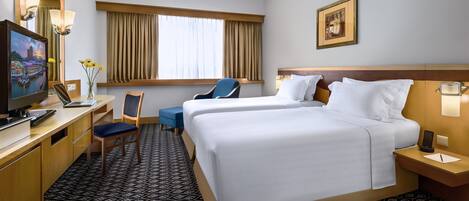 A hotel room with two beds, a desk with a computer, a chair, a television, and a window with curtains.