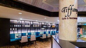 Tiffany Cafe & Restaurant met een modern interieur, met een marmeren kolom, blauwe zitplaatsen en een etalage met diverse artikelen op planken.