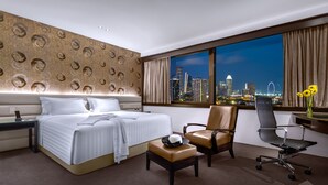 Een hotelkamer met een bed, een bureau, een stoel en uitzicht op een stadsbeeld 's nachts.