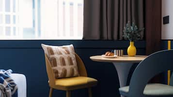 A modern room with a yellow chair, a round table with a yellow vase and pastries, and a window with curtains.