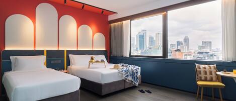 A hotel room with two beds, a city view, and a dining area with a table and chair.